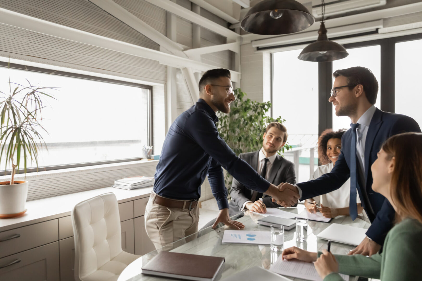 Diverse business partners shaking hand in modern boardroom after negotiation, signing contract, making successful deal, Arabian executive greeting new employee at meeting, group negotiations